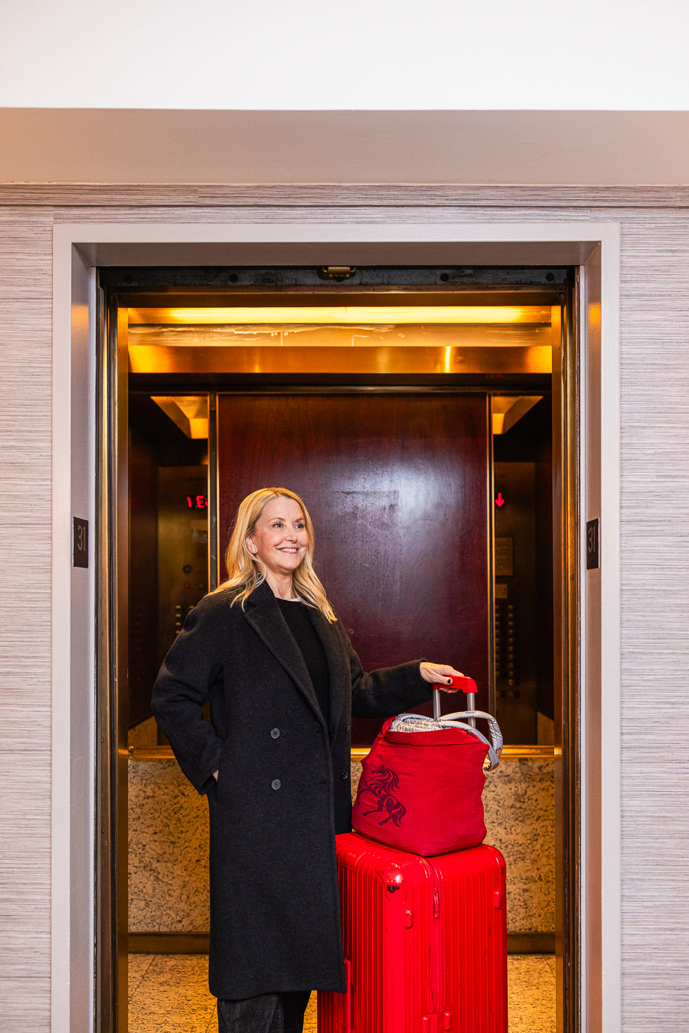 Woman with a red suitcase entering an elevator.